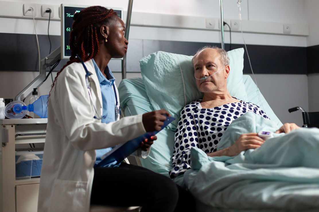 A bilingual nurse speaking with an elderly patient in a hospital bed, demonstrating compassionate care and effective communication in a Canadian healthcare setting.