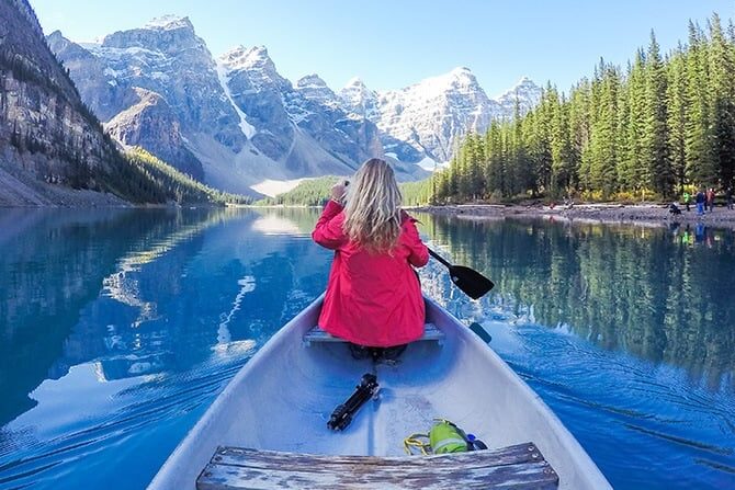Travel nurse paddling a canoe on a turquoise lake with mountains and pine trees in Alberta, Canada.