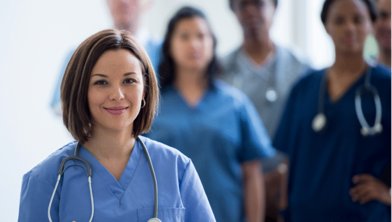 A smiling bilingual nurse standing confidently in front of a diverse medical team, representing the importance of communication and cultural connection in Canadian healthcare.