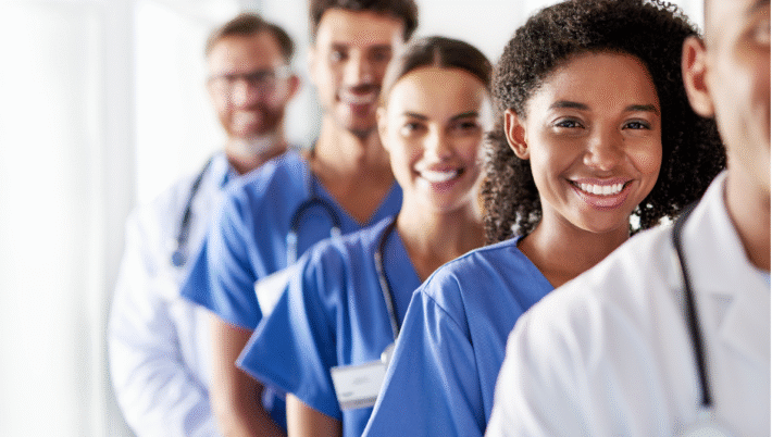 Group of smiling healthcare professionals in scrubs and lab coats standing in a line, representing teamwork in Canadian travel nursing